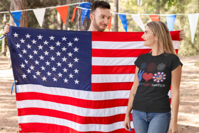 Peace Love America Sunflower 4th of July America Flag Hippie T-Shirt - Happy Patriotic 4th July Day-t-shirt-mockup-of-a-blond-woman-standing-next-to-an-american-flag