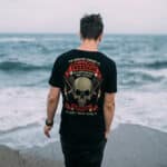 Smiling guy in a black T-shirt stands on the sandy seashore.