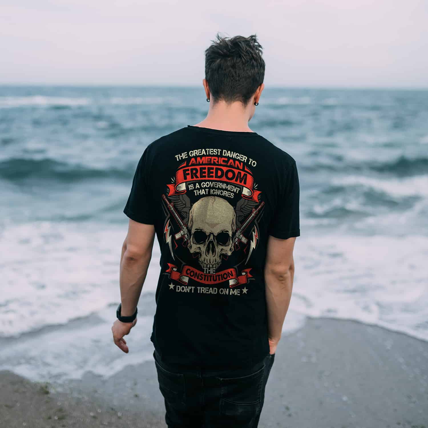 Smiling guy in a black T-shirt stands on the sandy seashore.